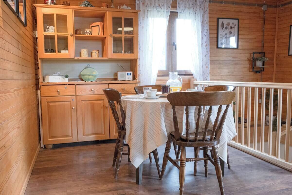 A wooden interior with a dining table, chairs, a cabinet with glass doors, and a window with curtains.