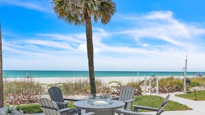 Un patio frente a la playa con una mesa redonda y cuatro sillas Adirondack, con vistas al océano.