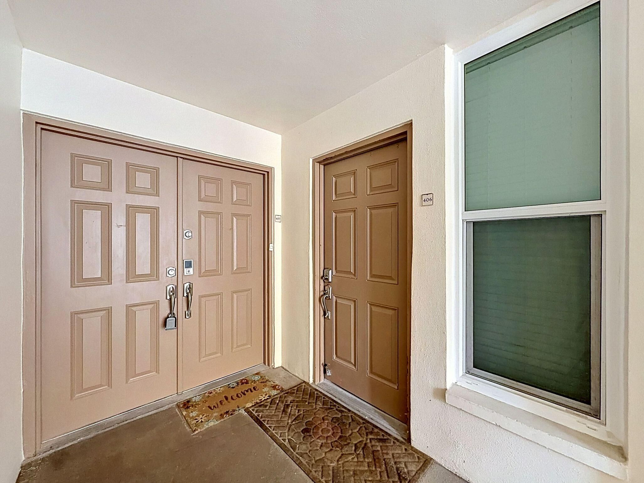 A hallway with two brown doors, a welcome mat, and a window with a green view.