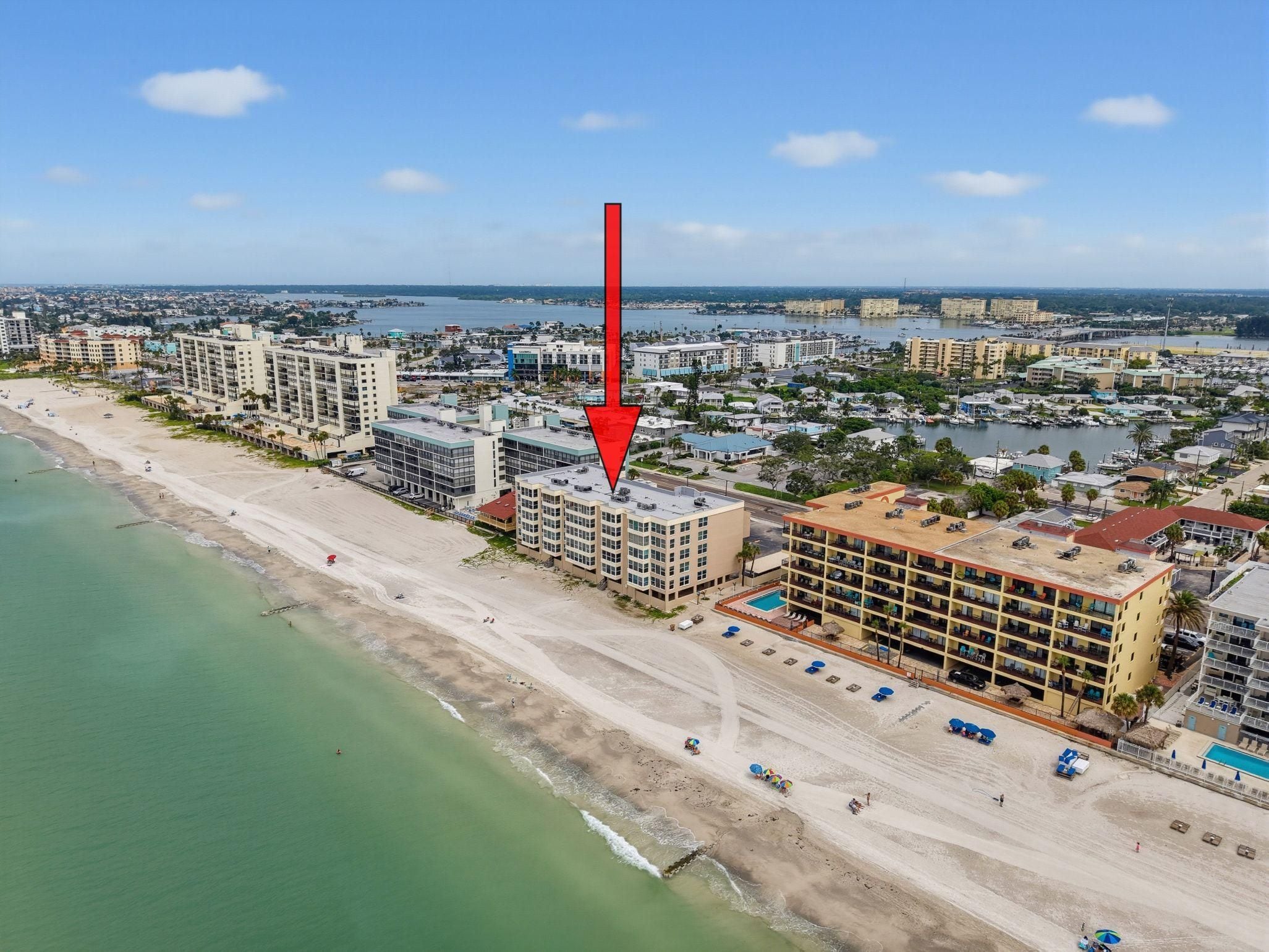 Vista aérea de una ciudad costera con un hotel frente a la playa, con varios pisos, piscina y vista al océano.