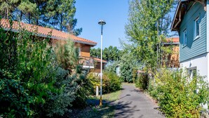 A pathway leading to a building with a tiled roof, surrounded by greenery and trees. - Large Nature Retreat for 8 by the Lake (Parentis-en-Born)