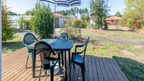 A deck with a table and chairs, an umbrella, and a view of houses and trees. - Large Nature Retreat for 8 by the Lake (Parentis-en-Born)