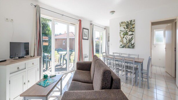 A living room with a sofa, TV, dining table, and chairs. - Large Nature Retreat for 8 by the Lake (Parentis-en-Born)