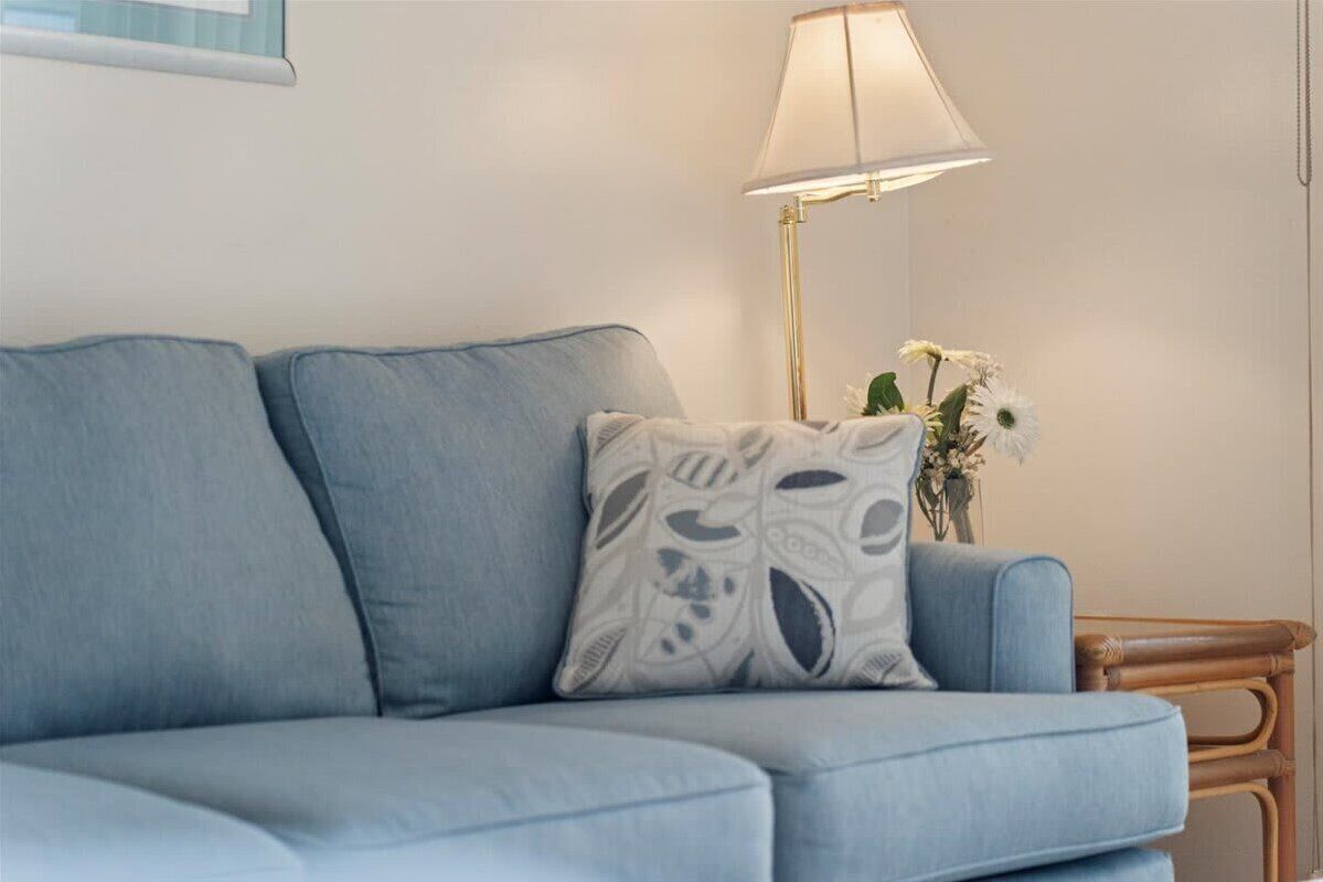 A light blue sofa with a patterned pillow, a floor lamp, and a small table with flowers.