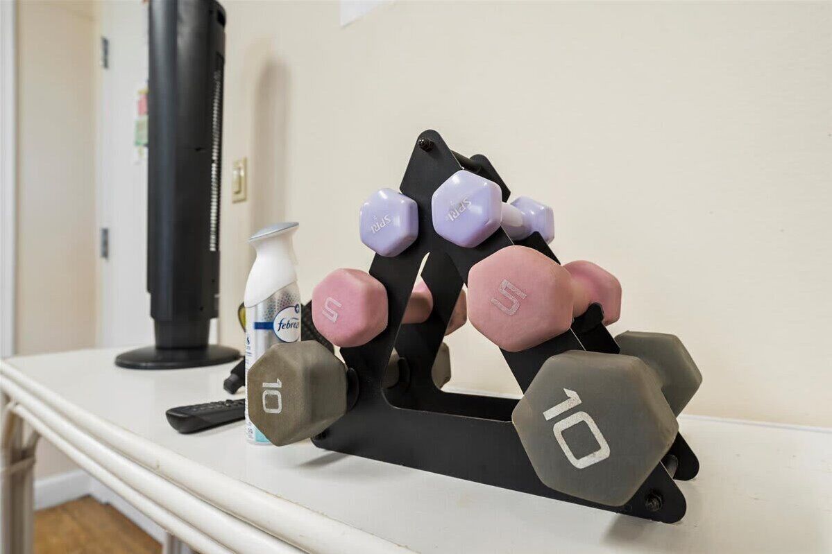 A weight bench with dumbbells, a water bottle, and a black cylindrical object on a white table.