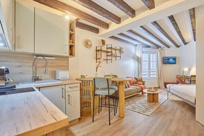 A modern kitchen with wooden beams, a dining area with chairs and a table, a sofa, and a TV in a living room. - Apartement Saint Germain des Pres (Paris)