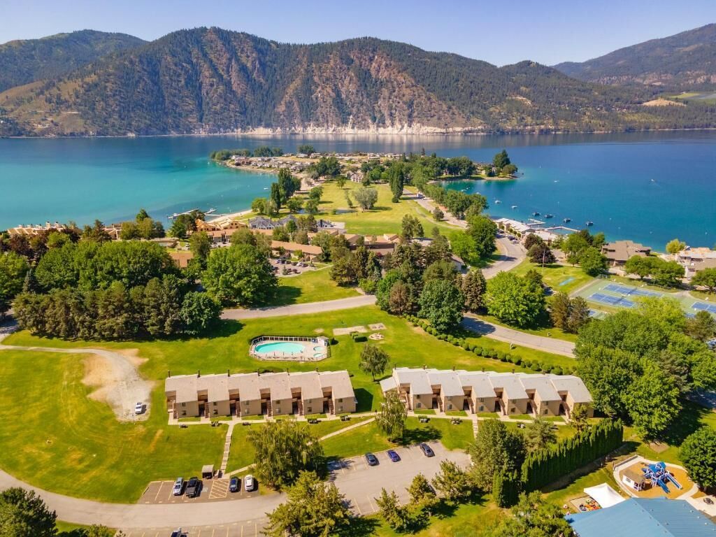 An aerial view of a resort with multiple buildings, a swimming pool, and a lake with mountains in the background.