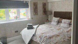 A bedroom with a bed, a window, a chandelier, and a wall with leaf-patterned decor. - Tranquil Solihull Retreat - 3 Bedroom House (Solihull)