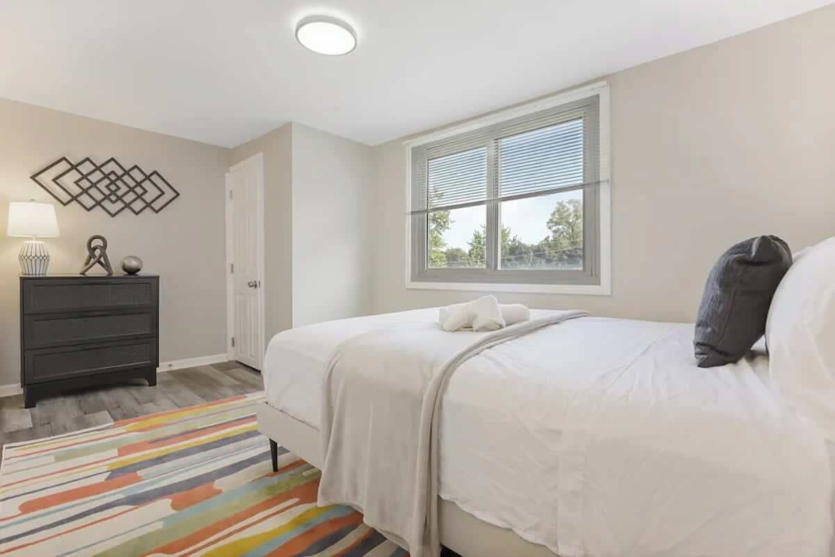 A bedroom with a bed, a dresser, a window with blinds, and a decorative wall piece.