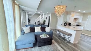 A modern living room with a sectional sofa, ottoman, and a kitchen area with a bar. - Spacious 5 Bed 2 bath House (Melrose Park)