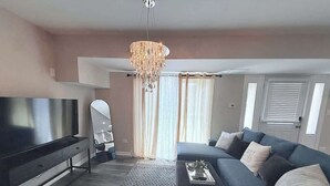 A living room with a TV, sofa, and chandelier. - Spacious 5 Bed 2 bath House (Melrose Park)