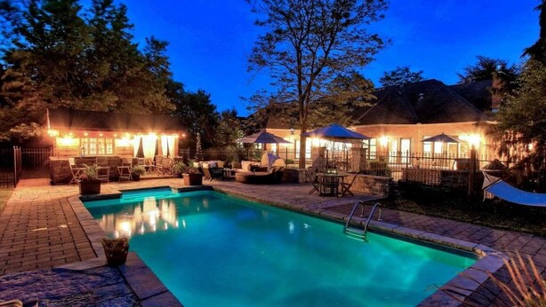 A swimming pool with lounge chairs and umbrellas, surrounded by a brick patio and trees.
