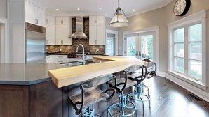 A modern kitchen with a central island, bar stools, a stainless steel refrigerator, and a clock on the wall.