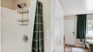 A bathroom with a shower, a towel rack, and a door leading to a bedroom with a bed and a window. - Sunny Mt. Tabor Studio, Full Kitchen, Walk to Parks (Portland)