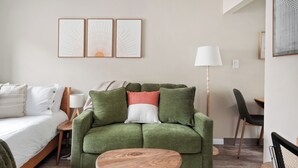 A room with a green sofa, a wooden coffee table, a bed with white bedding, a desk with a chair, and three framed artworks on the wall. - Sunny Mt. Tabor Studio, Full Kitchen, Walk to Parks (Portland)