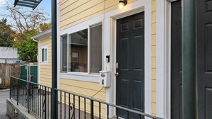 A residential building with a black front door, a mailbox, and a small porch with a metal railing. - Sunny Mt. Tabor Studio, Full Kitchen, Walk to Parks (Portland)