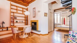 Un salon moderne avec une cheminée, un plancher en bois, une table ronde avec des chaises, une bibliothèque et un canapé coloré.