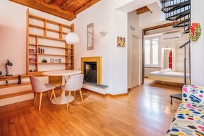 Ein modernes Wohnzimmer mit Kamin, Holzböden, einem runden Tisch mit Stühlen, einem Bücherregal und einem farbenfrohen Sofa.