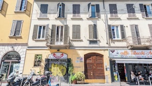 Une rangée de bâtiments aux fenêtres fermées par des volets, une porte en bois close et une devanture de magasin avec une enseigne.