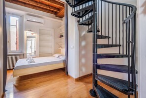 Ein Schlafzimmer mit einem Bett, einem Fenster, einer Heizung und einer Wendeltreppe.