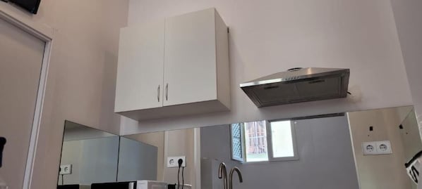 A kitchen with white cabinets, a stainless steel range hood, and a window with a view. - Hostal Andrea Sol (Madrid)