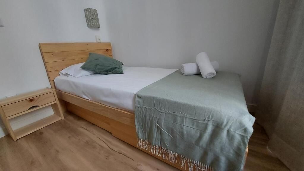 A single bed with a wooden headboard, a green pillow, and a white blanket.