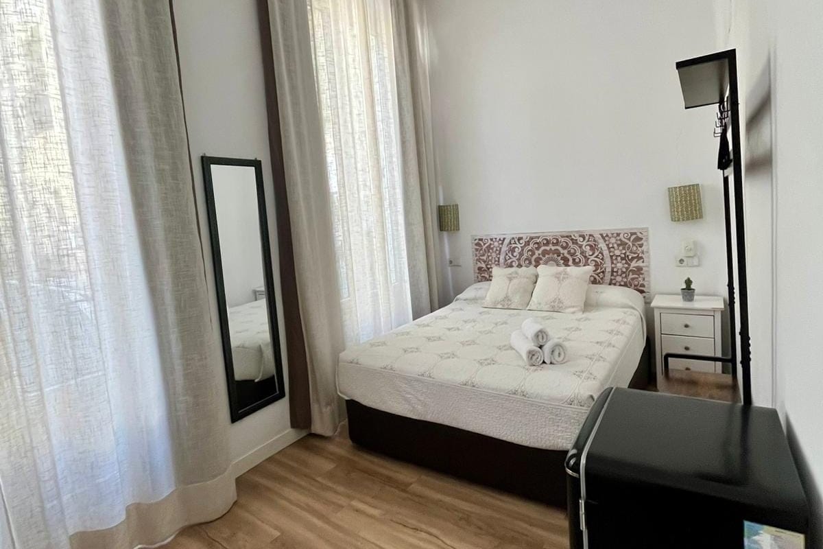 A bedroom with a bed, a ceiling fan, a bedside table, a lamp, and a black speaker.