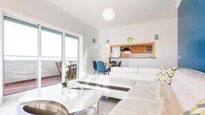 A modern living room with a sofa, a coffee table, and a dining area with chairs. There is a large window providing a view outside. - Tatiana Apartment - Located in one of the most prestigious areas of Portimão. (Portimão)