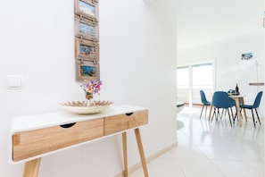 Een moderne kamer met een wit bureau, een bloevas en een zithoek met blauwe stoelen.