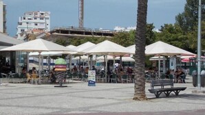 An outdoor seating area with umbrellas, tables, and chairs, surrounded by palm trees and buildings. - Tatiana Apartment - Located in one of the most prestigious areas of Portimão. (Portimão)