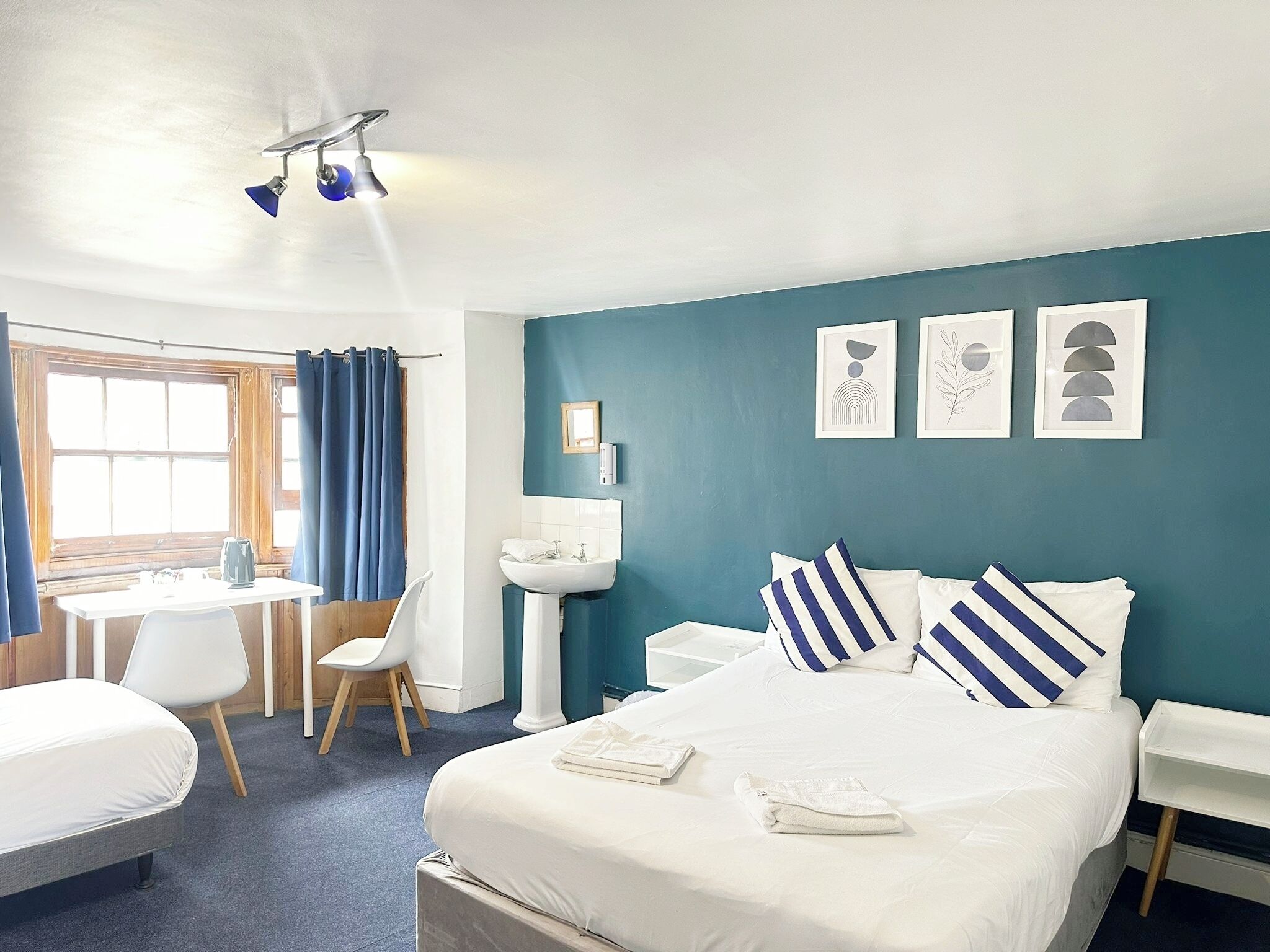 A hotel room with a bed, a desk, a chair, a sink, and a window with curtains.