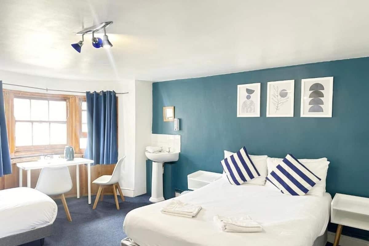 Une chambre d’hôtel avec un lit, un bureau, une chaise, un lavabo et des œuvres d’art accrochées au mur.