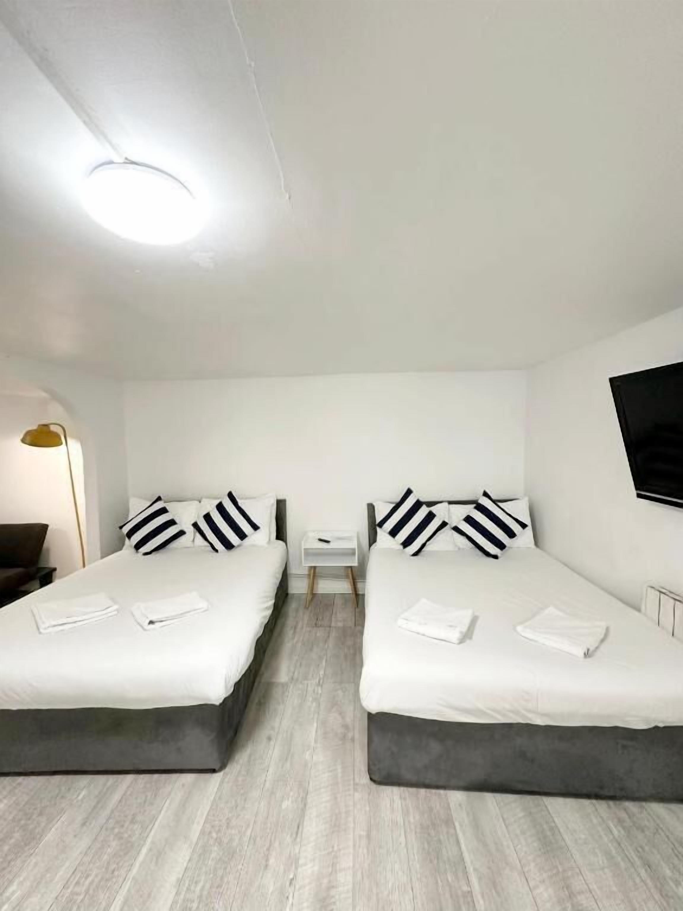 A hotel room with two beds, a small bedside table, a lamp, and a TV.