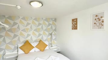 A hotel room with a bed, a geometric-patterned wall, a ceiling light, and two framed artworks.