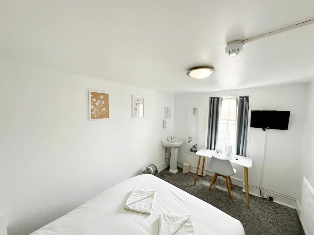 A hotel room with a bed, a desk, a chair, a sink, and a television.