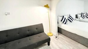 A modern room with a sofa, a floor lamp, and a bed with striped pillows. - Number 75 (Brighton)