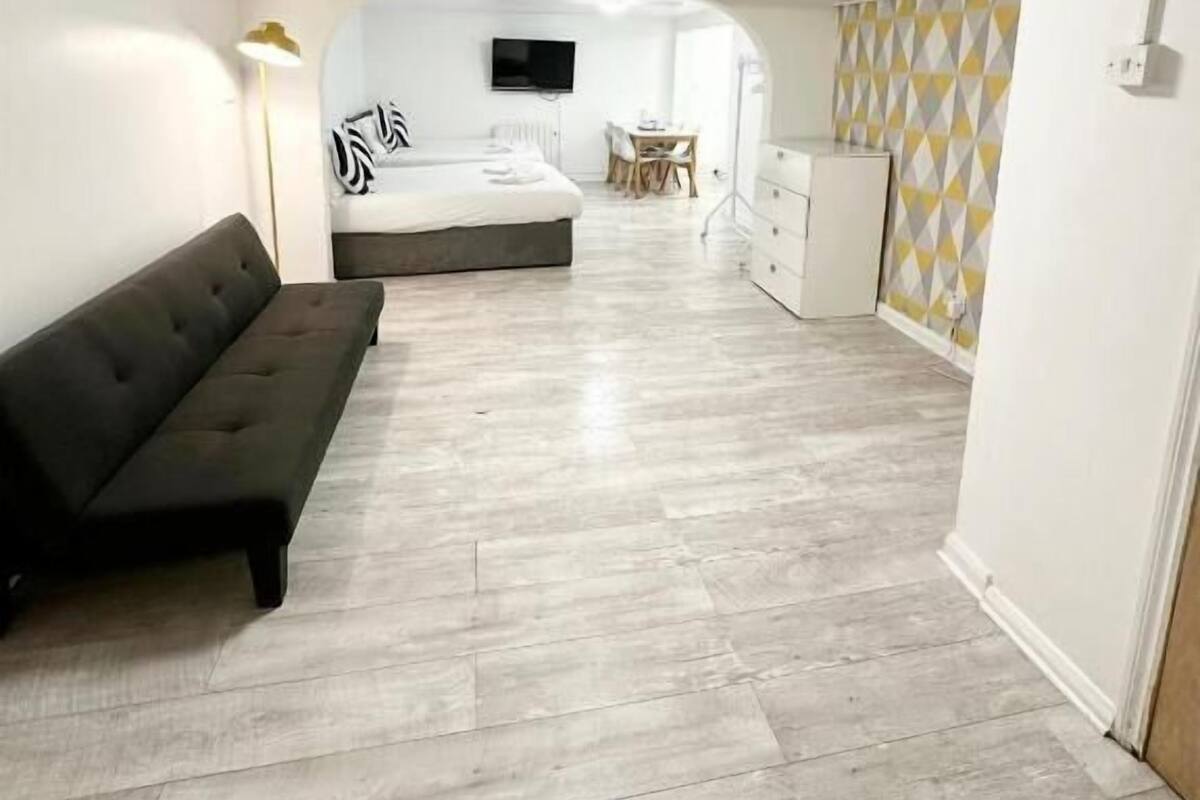 Une chambre d’hôtel moderne avec un canapé, un lit, une télévision, une petite table et un mur décoré de motifs.