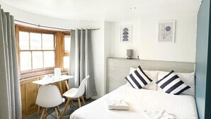 A hotel room with a bed, a desk, two chairs, a window with curtains, and two wall-mounted artworks. - Number 75 (Brighton)