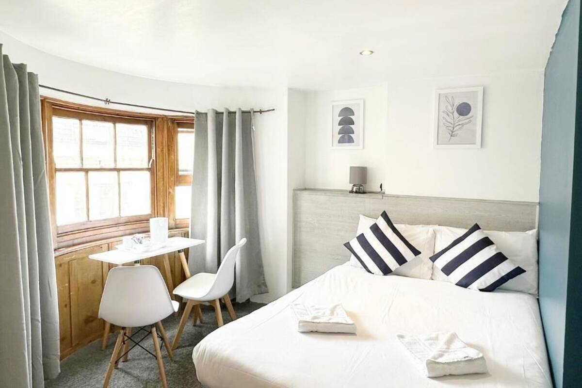 Une chambre d’hôtel comprenant un lit, un bureau, deux chaises, une fenêtre avec des rideaux et deux œuvres d’art accrochées au mur.
