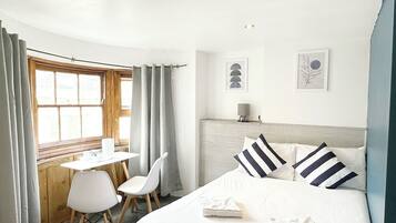A hotel room with a bed, a desk, two chairs, a window with curtains, and wall art.