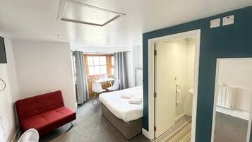 A hotel room with a bed, a red sofa, a fan, a shower, and a view of the outside.