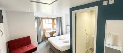 Habitación de hotel con cama, sofá rojo, ventilador, ducha y vistas al exterior.