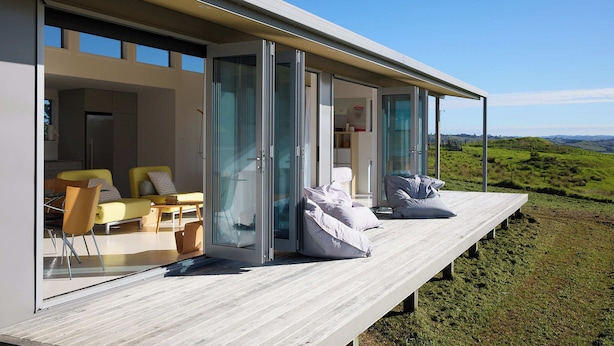 Et moderne udendørs opholdsområde med træterrasse, møbler og glasdøre, der fører ind i et rum.