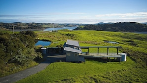 Et moderne hus med en terrasse med udsigt over en sø, omgivet af frodige grønne marker.