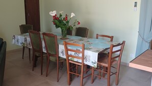 A dining area with a table set for four, surrounded by wooden chairs, a vase with flowers, and a wooden ceiling with exposed beams. - "At grandpa's" (Limalonges)