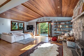 A spacious living room with a white sofa, wooden flooring, a stone fireplace, and a bookshelf. - Horizon House | Hot Tub, Views, Gardens + Golf (Sebastopol)