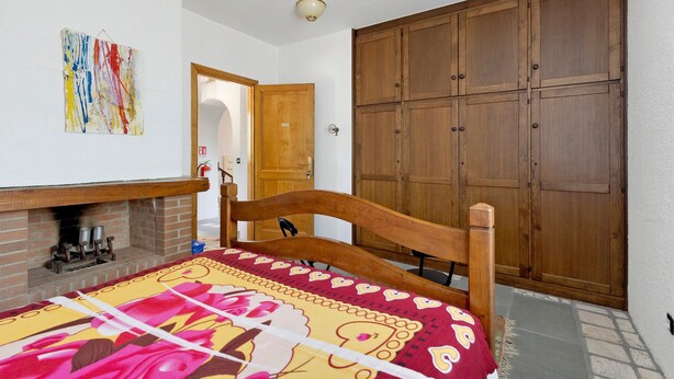 Ein Schlafzimmer mit einem hölzernen Bett, einem Kamin, einem Kleiderschrank und einem farbenfrohen Kunstwerk an der Wand.