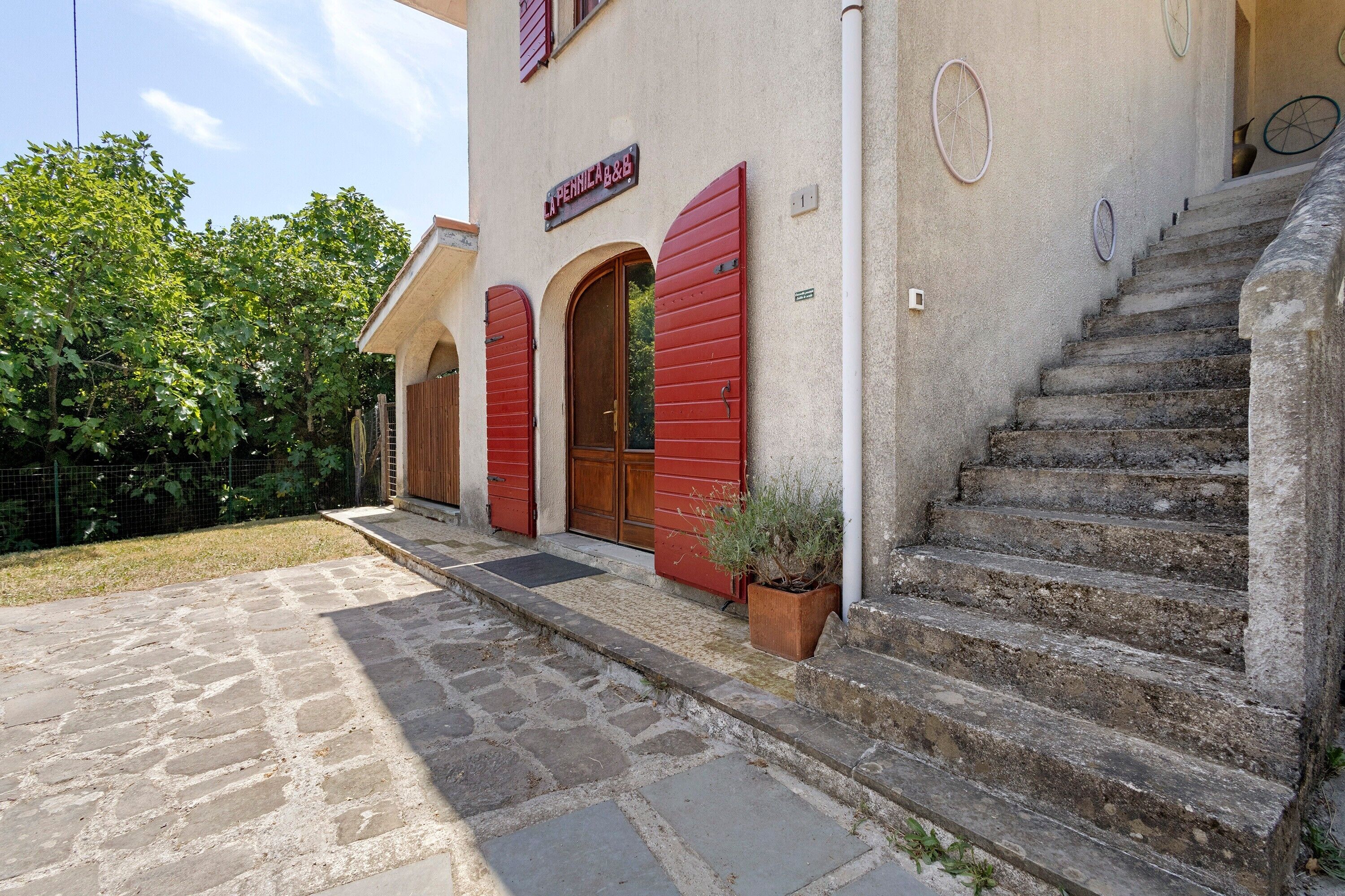 Un edificio con ingresso in pietra, persiane rosse e un cartello con la scritta 'LA PENNICA B&B'.