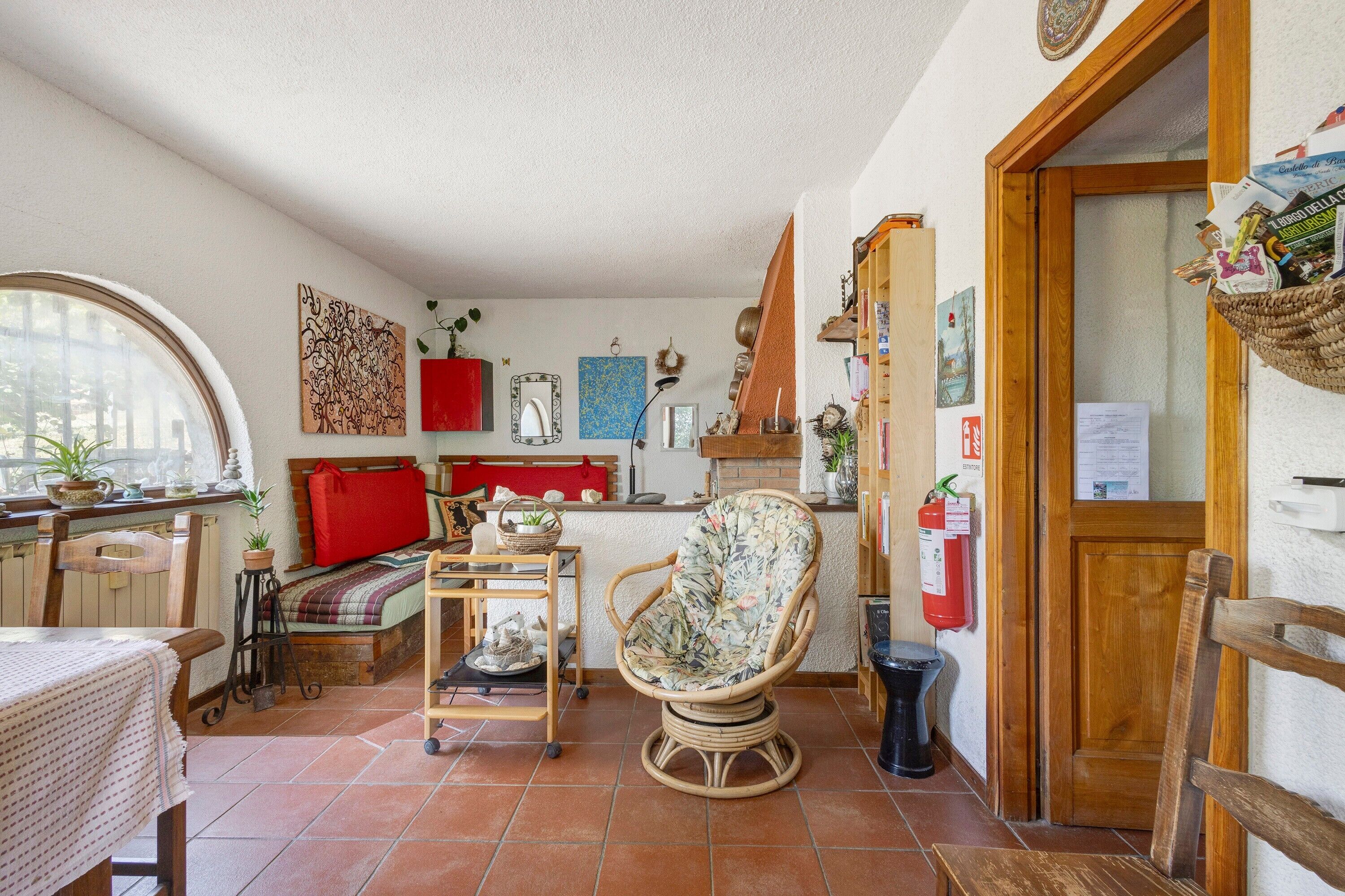 Una stanza accogliente con un letto, una poltrona in vimini, un tavolino e una mensola con diversi oggetti.
