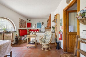 Ein gemütliches Zimmer mit einem Bett, einem Korbstuhl, einem kleinen Tisch und einem Regal mit verschiedenen Gegenständen.